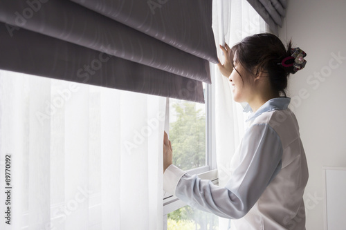 Young woman opening curtains in bedroom