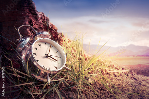 Alarm clock on grass at sunset or sunrise/ time concept