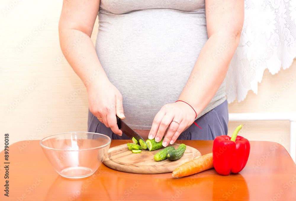 Pregnant woman cuts the cucumber. Diet for pregnant women.