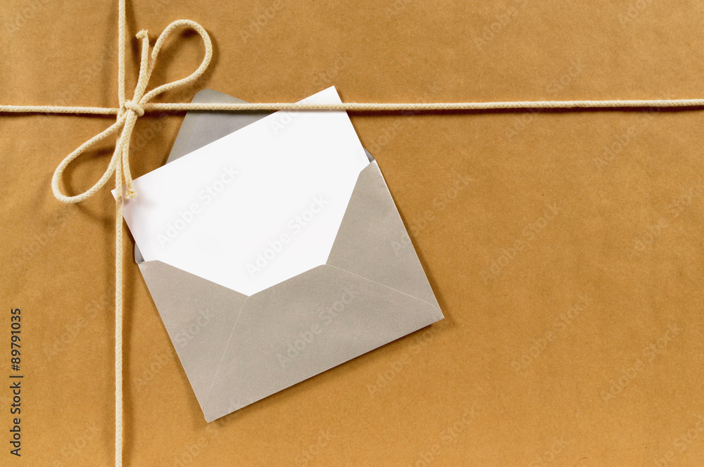 Fototapeta premium Brown paper parcel or wrapped package background with greeting card message label or gift tag in silver envelope photo