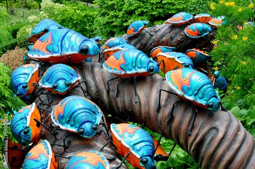 Cement bugs art climbing on the tree in a public park.