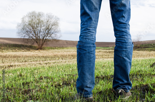 Man stands on burnt field with some remains of green grass and lonely tree on it. Nature background.