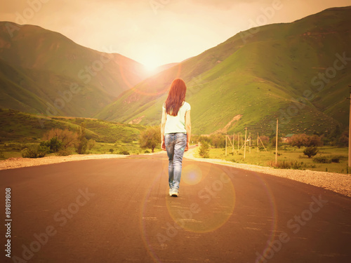 Little girl child walking on road to mountains at sunset