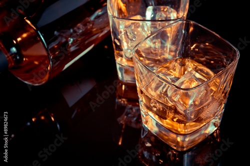 top of view of glass of whiskey near bottle on black table with reflection, old style photo