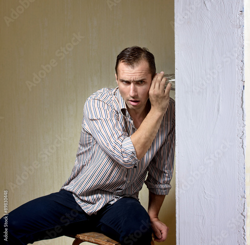 Man with a glass listening to a conversation through the wall