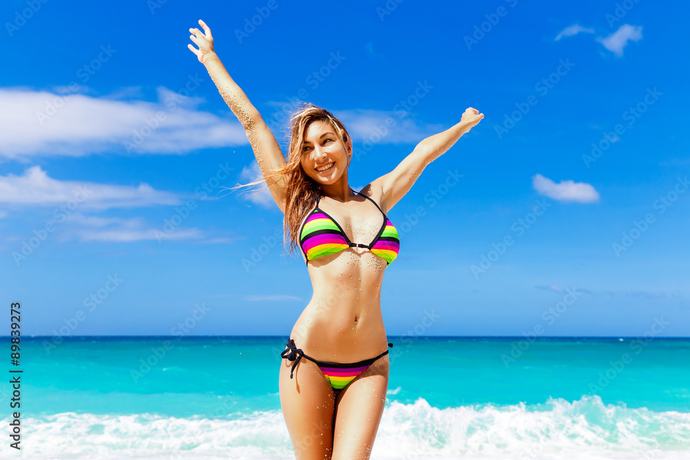 Naklejka premium Beautiful young girl in bikini on a tropical beach. Blue sea in