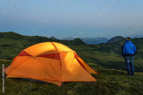 Mann steht in der Abenddämmerung vor seinem Zelt