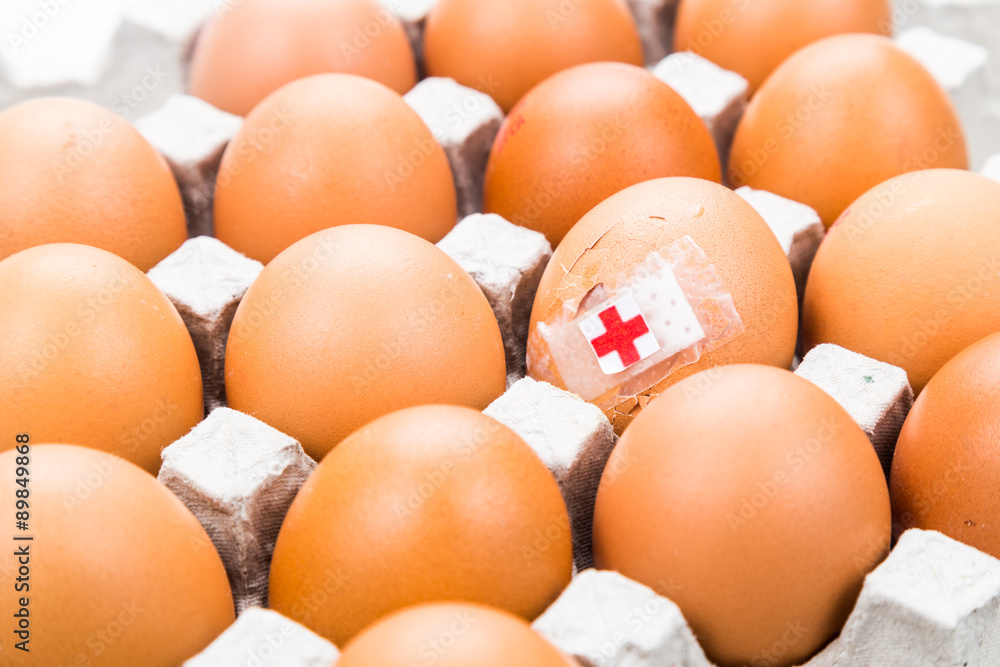 Concept of cracked egg with bandage placed with other eggs on tr Concept of cracked egg with bandage placed with other eggs on tr