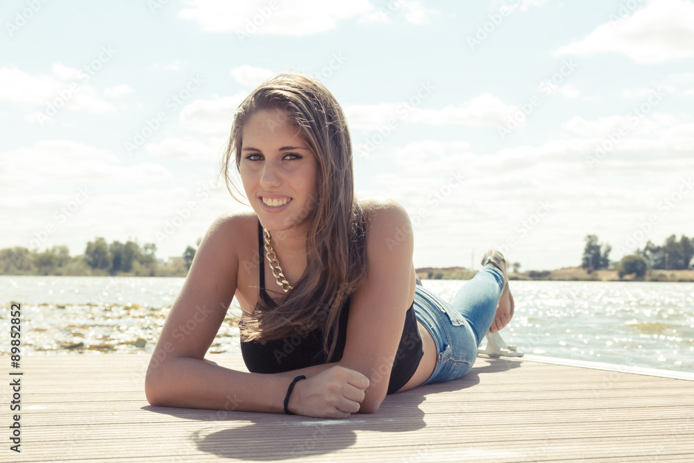 Chica adolescente posando en el embarcadero. Adolescente rubia de quince años como modelo. Chica rubia de pelo largo al lado del rio en verano.