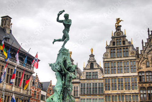 The city hall on the central market place in Antwerp in Belgium, with many flags and the statue in front of it together with some typical buildings 
