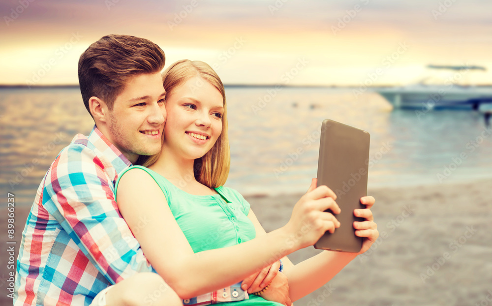 couple with tablet pc taking selfie over beach