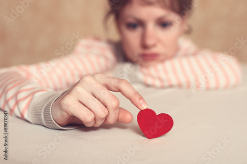 Upset and sad girl is touching heart symbol with finger