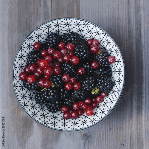 bowl with wild backberries and redcurrants on a hardwood table