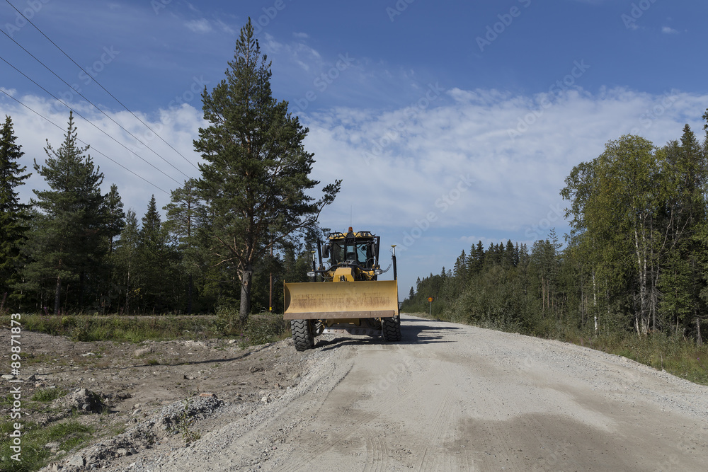 A parked grader on a road with some trees A parked grader on a road with some trees