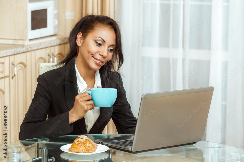 Businesswoman with cup of coffe using laptop in kitchen