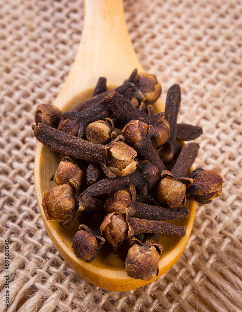 Obraz premium Heap of cloves with wooden spoon on jute canvas, seasoning for cooking
