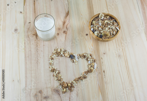 Heart-shaped muesli, bowl of muesli and glass of milk on the wooden table.