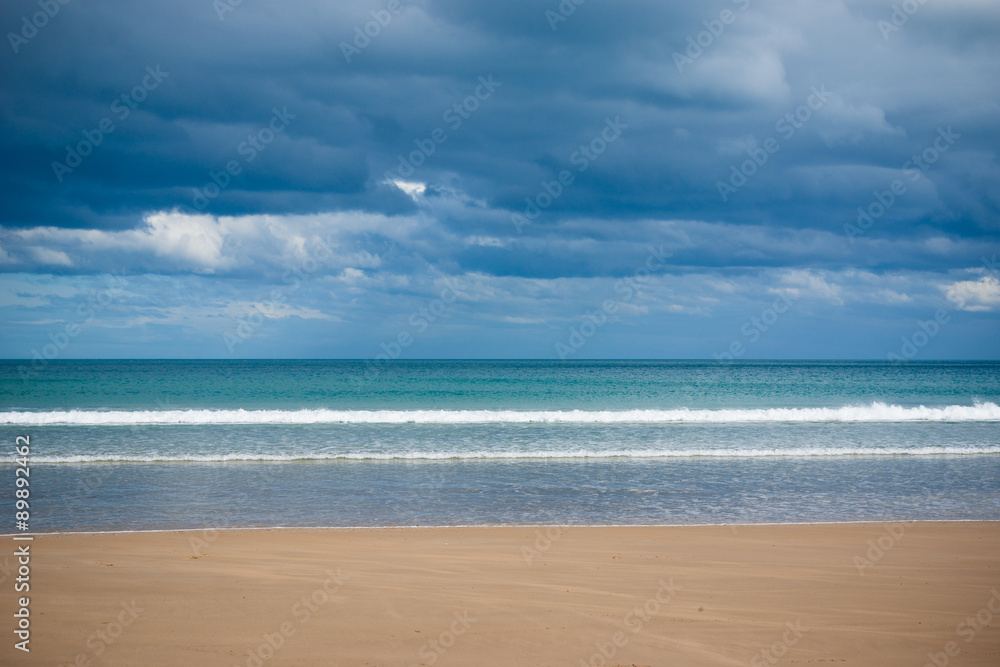 Small waves break on a sandy beach on a stormy day