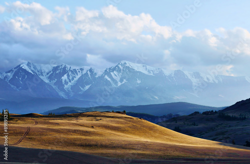 Beautiful evening landscape with sunny valley and snowy mountains in the distance