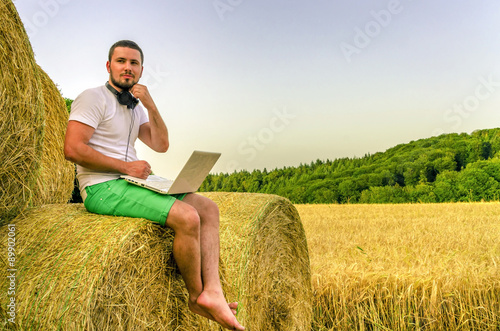 Country man with a laptop sitting on the hay. © Alex Tor