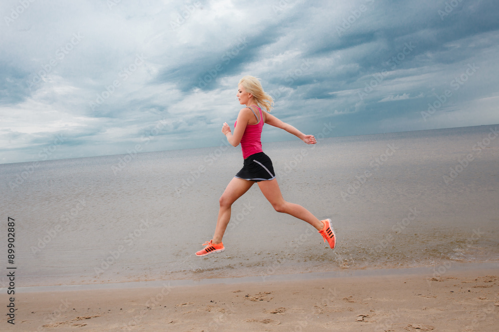 Blond female in sportswear running near the sea over blue sky wi Blond female in sportswear running near the sea over blue sky wi