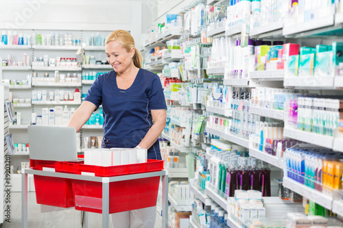 Chemist Using Laptop On Medicine Basket In Pharmacy