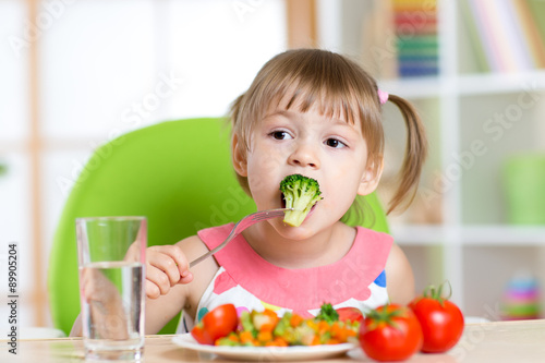 Cute little girl eats vegetable salad using fork