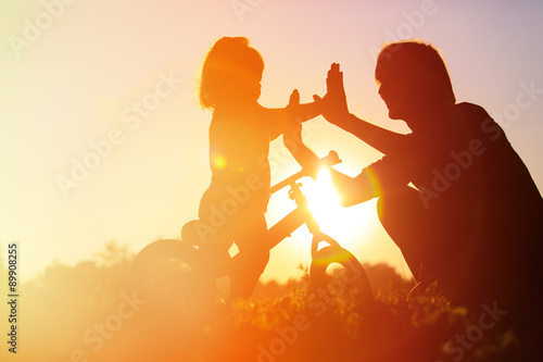 father and daughter having fun riding bike at sunset