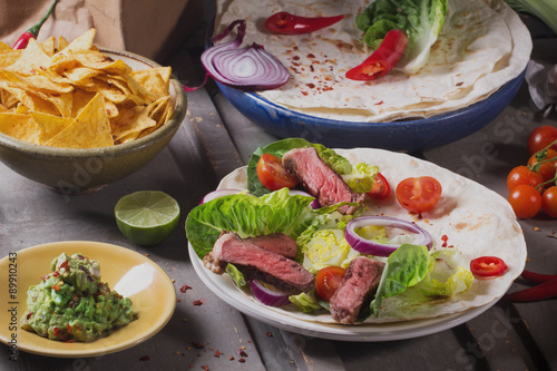 Mexican tortillas with green fresh salad filling, beef, onions, tomatoes with gucamole and tortilla chips on te vintage board photo