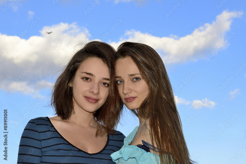 Two beautiful young women standing over blue sky and hugging Two beautiful young women standing over blue sky and hugging