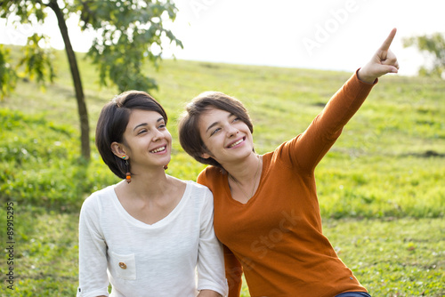 Two young women in a park one of them points at something