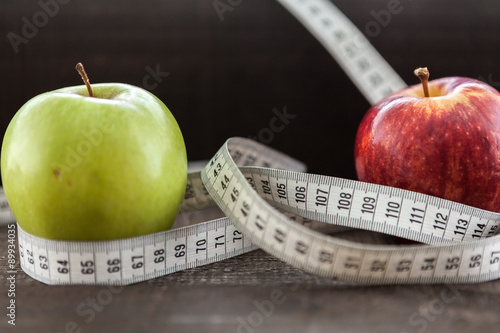  apple surrounded by a measuring tape referring to diet and health concept on wooden background