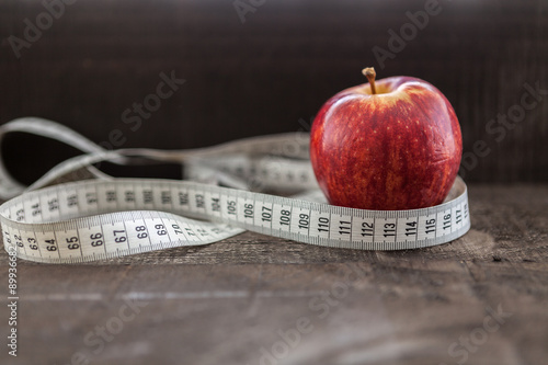  apple surrounded by a measuring tape referring to diet and health concept on wooden background