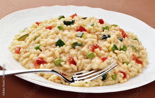 Dish of risotto zucchini peas tomatoes with fork