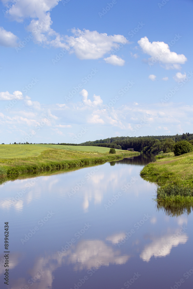 A beautiful landscape from Finland. Image taken during a warm sunny day and some clouds are in the sky and making a reflection in the still water.