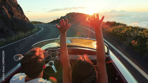Couple driving convertible car. steadicam shot with flare into sunset in Hawaii photo