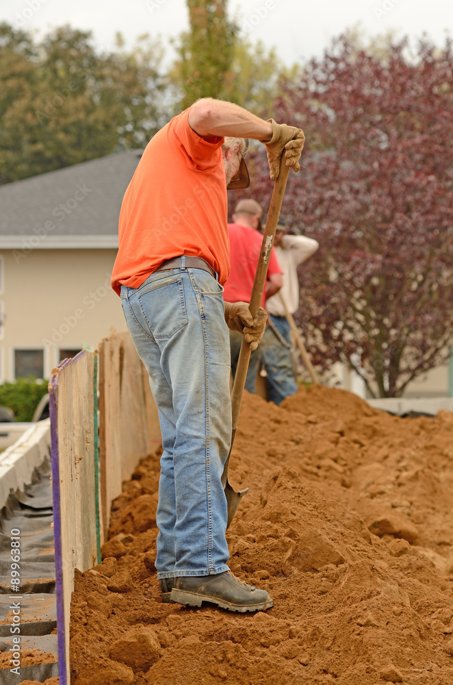 Contractor working on building site installing a retaining wall and working on back fill.