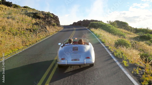 Happy Couple Driving Classic Convertible Car into Sunset on Country Road. Romantic Freedom Relaxing Road Trip Concept. Steadicam Shot.