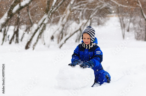 little boy building snowman in winter park