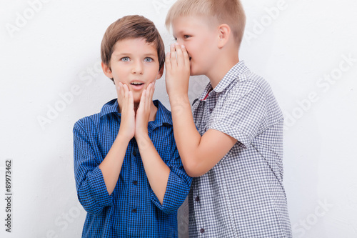 Teenage boy whispering in the ear a secret to friendl on white photo