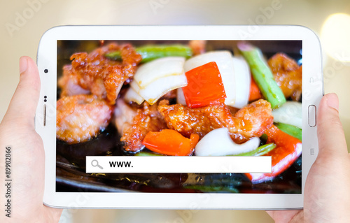 Hand holding tablet with www. word on search bar over food backg