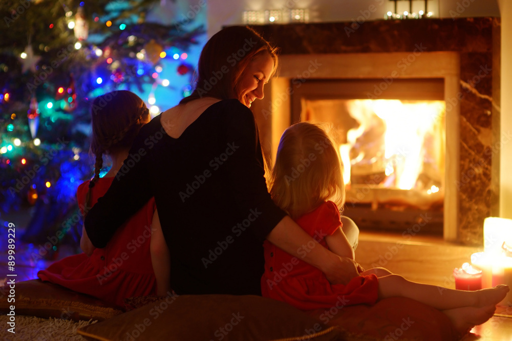 Young mother and daughters sitting by a fireplace on Christmas