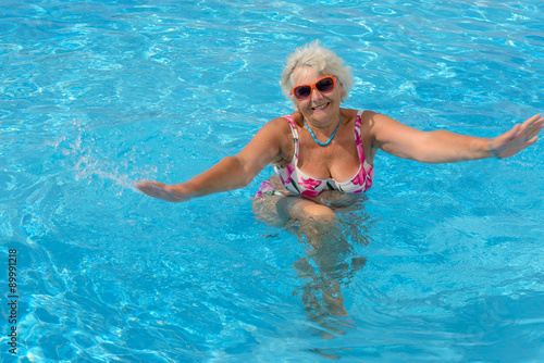 Aged woman is doing spa exercises in bright blue water of pool. © vaz1