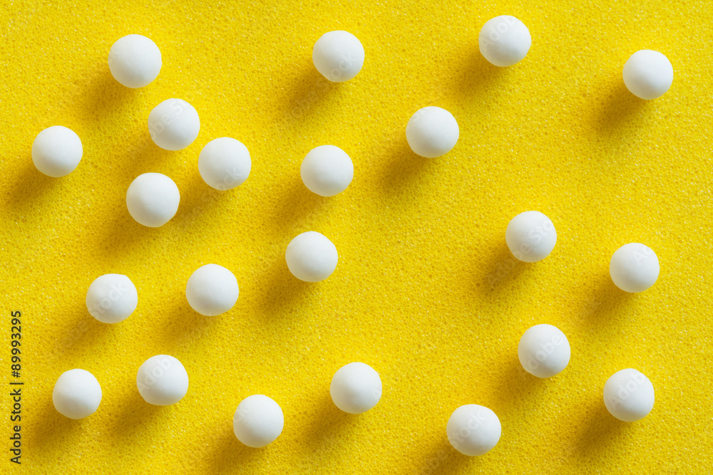 Homeopathic pills scattered - Overhead view of homeopathic pills (made from inert substance - sugar/lactose) scattered on a yellow surface. Natural light used. Homeopathic pills scattered - Overhead view of homeopathic pills (made from inert substance - sugar/lactose) scattered on a yellow surface. Natural light used.