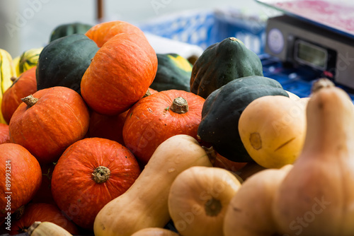 Cooking pumpkins, butternut squash and acorn squash at an October farmer's market, scales out of focus in the background.