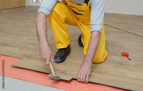 Laminate flooring of room, worker placing laminate plank 