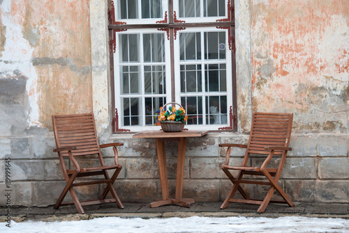 Table and two wooden chairs on the pavement in Tallinn Old Town Estonia. Snow can be seen on the pavement.