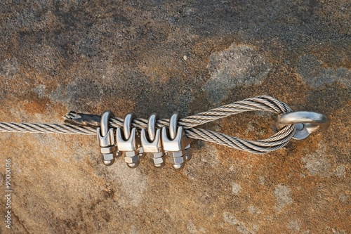 Solid knot on steel rope. Iron twisted rope fixed in block by screws snap hooks. Detail of rope end anchored into sandstone rock
