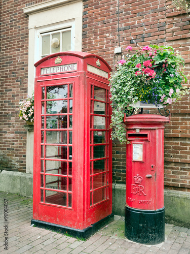 Traditional British red phone box andletterbox in pretty street with flowers.