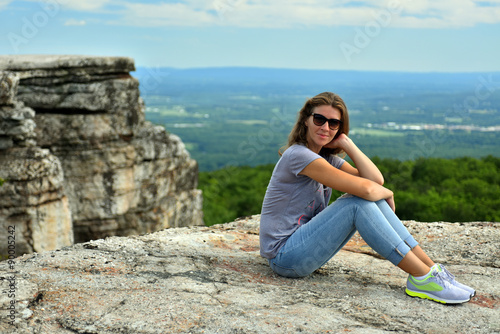 Young woman sitting at the edge of roc at Minnewaska State Park Reserve Upstate NY during summer time